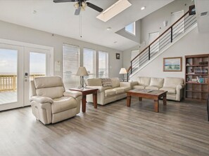 A spacious living room with a high ceiling, a staircase, and a view of the beach. - Brannen's Beachfront by Ryson Vacation Rentals (Galveston)