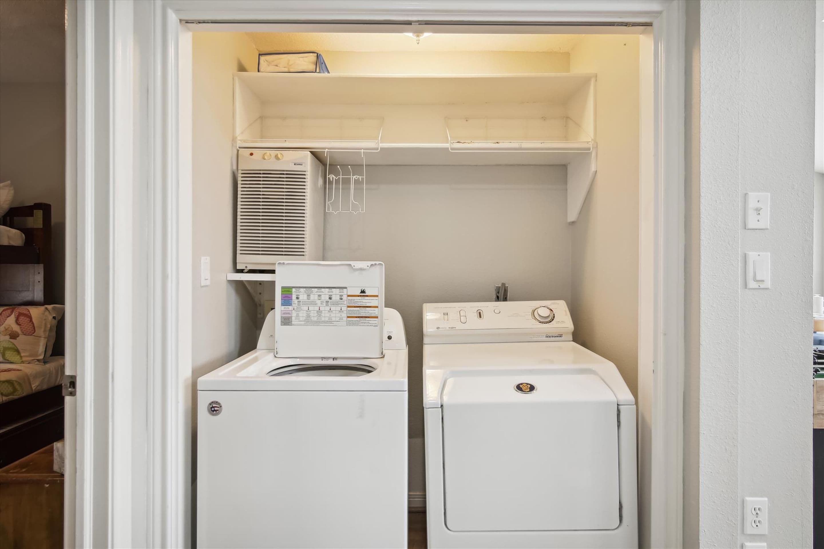 A compact laundry room with a front-loading washer and dryer, a small shelf above the dryer, and a vent above the washer.