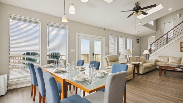A spacious living area with a dining table set for four, a sofa, and a staircase leading to an upper level. - Brannen's Beachfront by Ryson Vacation Rentals (Galveston)