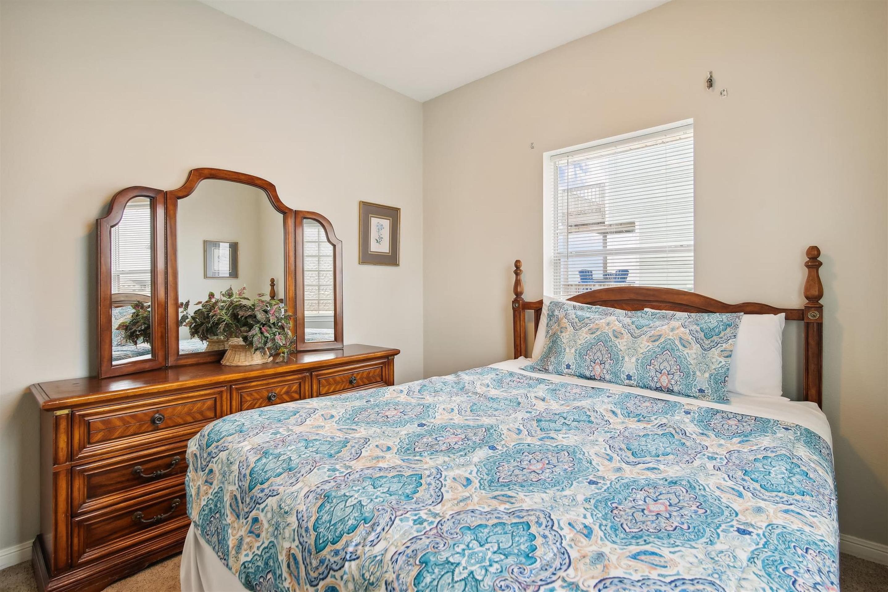 A bedroom with a wooden bed, a dresser with a mirror, and a window with blinds.