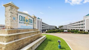 A hotel entrance with a sign for 'Casa de Mar Suites & Rentals' and a large building in the background.