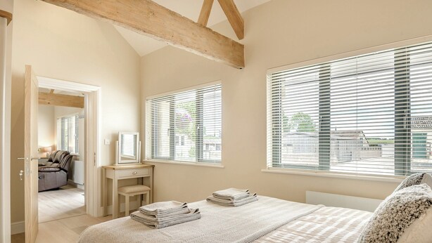A bedroom with a bed, a vanity with a mirror, and two windows with blinds. - The Ash - Arnolds Hill (Wingfield)