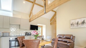 A modern kitchen with a dining area, a leather sofa, and a flat-screen TV. - The Ash - Arnolds Hill (Wingfield)