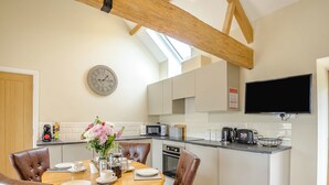 A modern kitchen with a dining area, featuring a wooden ceiling, a clock, and a flat-screen TV. - The Ash - Arnolds Hill (Wingfield)