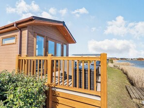 A wooden cabin with a deck, large windows, and a view of a lake.