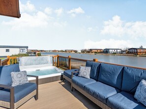 A deck with a hot tub, a sofa, and a view of a lake and buildings.