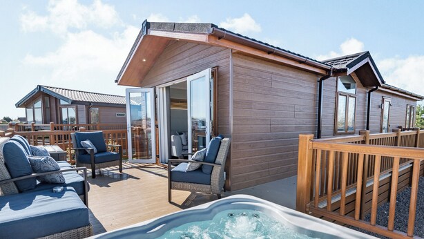 A hot tub, outdoor seating, and a wooden building with a glass door.