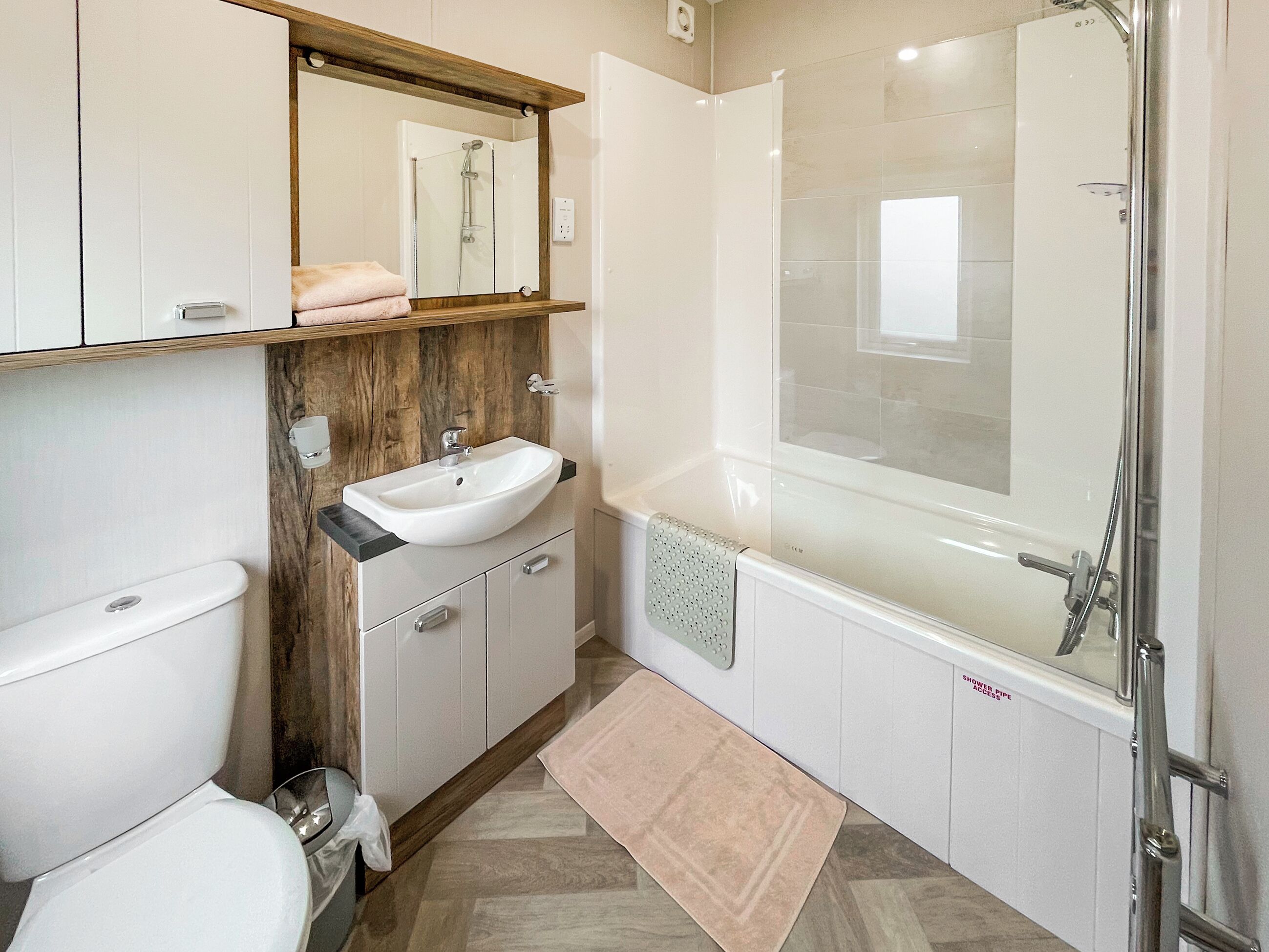 Et moderne badeværelse med toilet, vask, spejl, bruser og badekar.