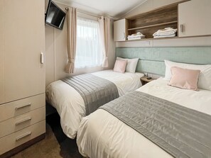 Une chambre avec deux lits, un téléviseur fixé au mur, une armoire et une fenêtre avec des rideaux.