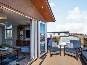Un salon moderne doté d’une grande porte-fenêtre coulissante donnant sur une terrasse, aménagée avec des canapés en osier et une table basse.