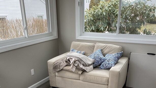 Ein Zimmer mit einem beigen Sofa, einem Fenster und Blick auf Bäume.