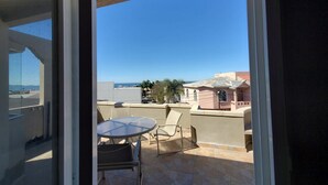 A balcony with a table and chairs, a view of the sea, and a building with a pink facade. - Lovely 2 Bdrm apartment with private terrace with grill (Tijuana)