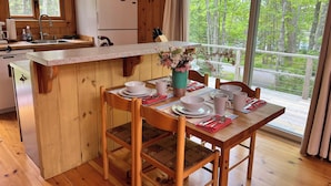 Cocina de cabaña de madera con comedor, un refrigerador, un lavamanos y una ventana con vista al bosque.