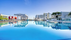 En klarblå pool med solstolar och parasoller, omgiven av moderna byggnader.