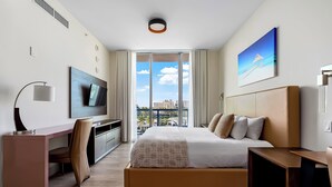 Ett modernt hotellrum med en stor säng, ett skrivbord, en TV och en balkong med utsikt över staden.