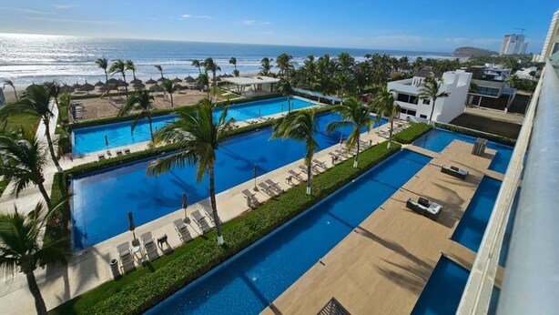 A resort with multiple swimming pools, palm trees, and a view of the ocean.