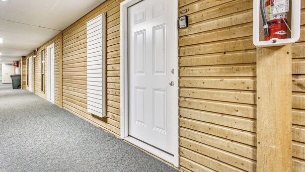 A hallway with wooden paneling, a white door, and a fire extinguisher mounted on the wall.