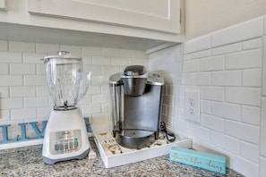 Une cuisine avec un plan de travail blanc, un mixeur et une machine à café.