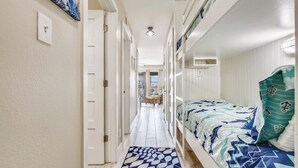 A narrow hallway with a bed on the right, a door on the left, and a patterned rug on the floor.
