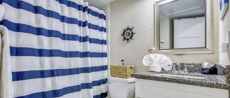 A bathroom with a striped shower curtain, a ship's wheel decoration, a toilet, and a sink with a mirror above it.