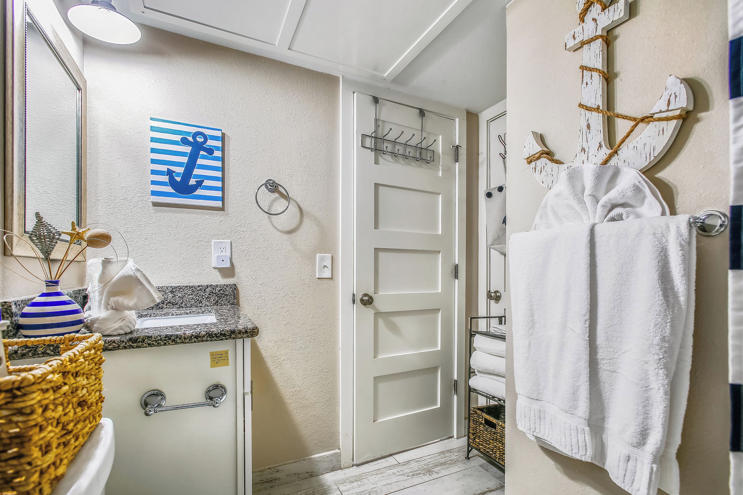 A bathroom with a white door, a towel rack with a white towel, a sink with a striped vase, and a decorative anchor on the wall.