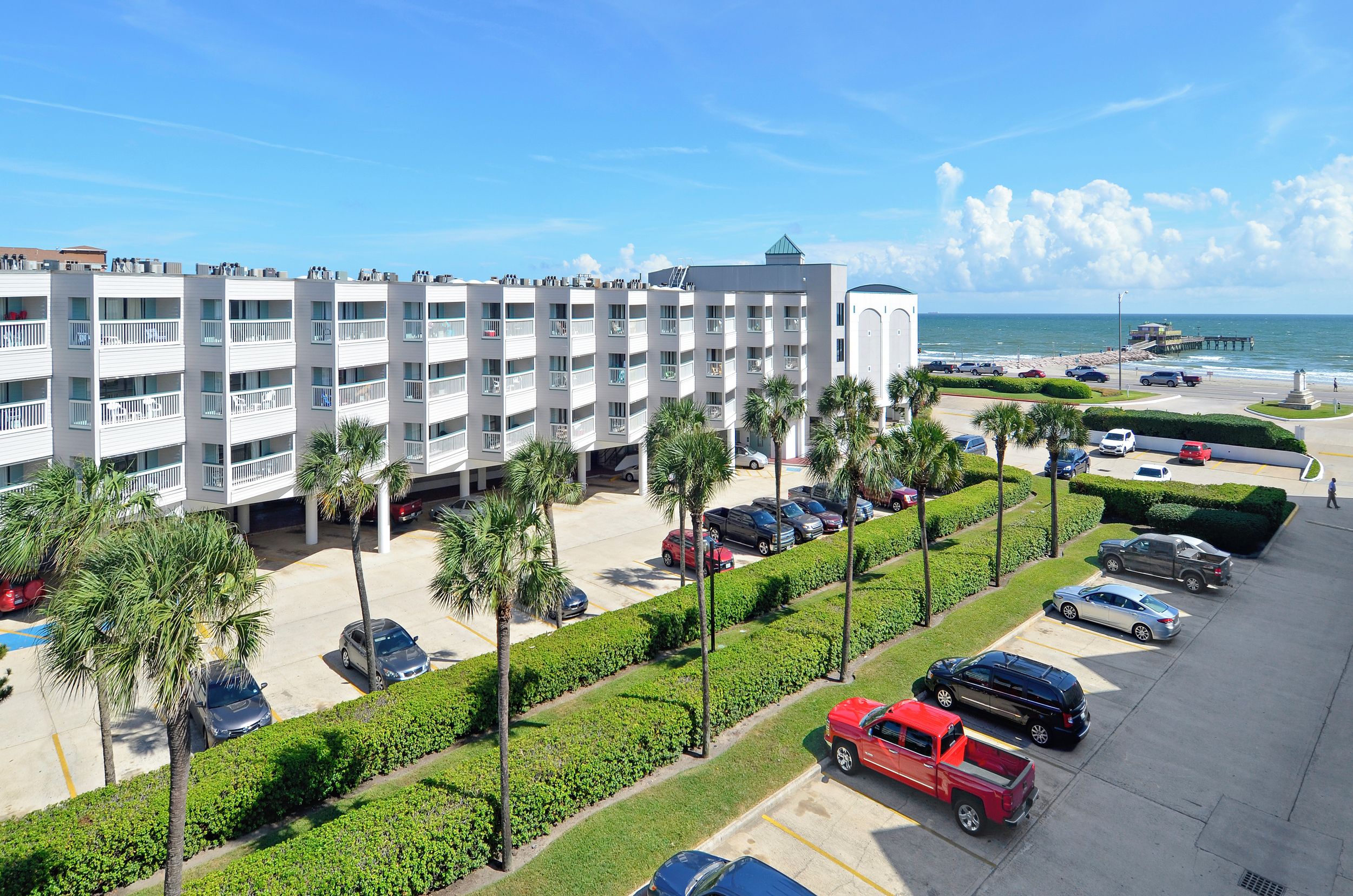 A multi-story hotel with a parking lot, palm trees, and a view of the beach.