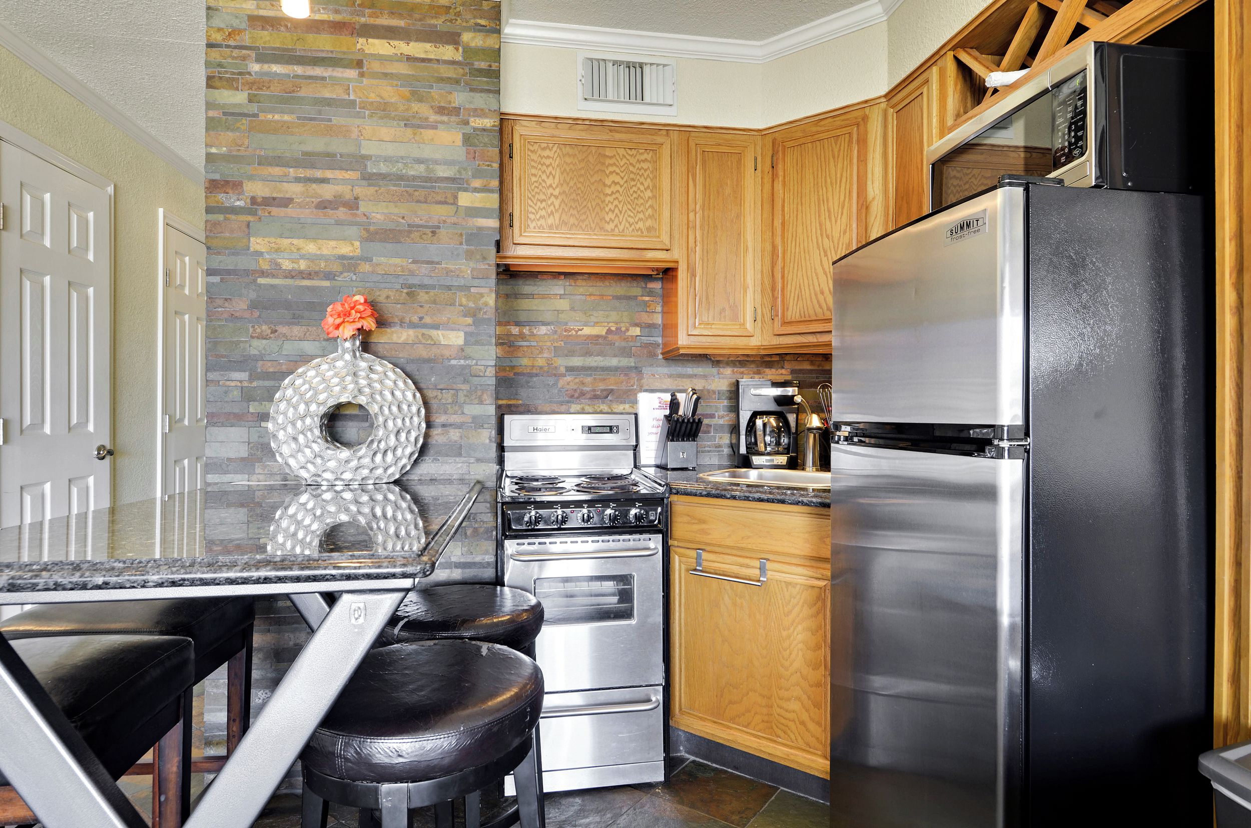 A kitchen with a stone backsplash, wooden cabinets, a stainless steel refrigerator, and a gas stove.