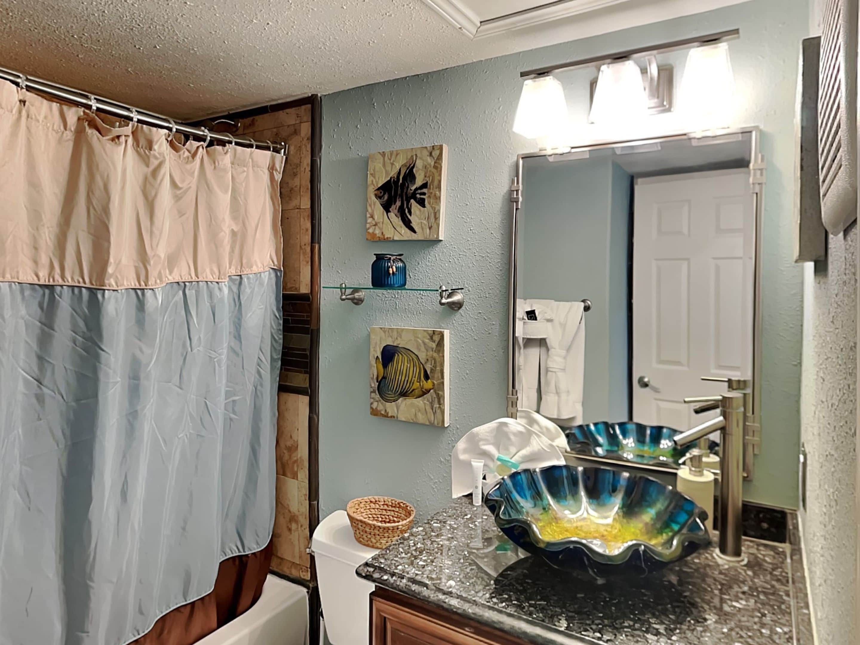 A bathroom with a shower curtain, a sink with a decorative bowl, and two wall-mounted fish paintings.