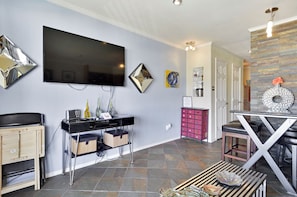 A modern living room with a flat-screen TV, a coffee table, and a dining area with a glass-top table and chairs.