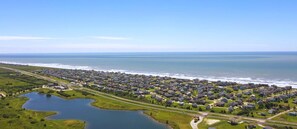 An aerial view of a coastal residential area with houses, a road, and a large body of water. - Casa Rosa West by Ryson Vacation Rentals (Galveston)