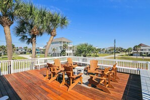 A wooden deck with outdoor furniture, palm trees, and a view of a residential area with houses. - Casa Rosa West by Ryson Vacation Rentals (Galveston)