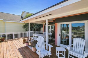 A covered outdoor patio with a table and chairs, a sliding glass door, and a wooden deck. - Casa Rosa West by Ryson Vacation Rentals (Galveston)
