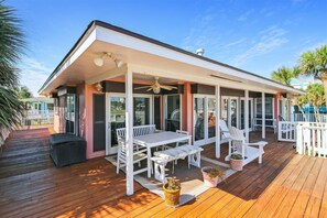 A covered outdoor deck with a white table and chairs, a ceiling fan, and potted plants. - Casa Rosa West by Ryson Vacation Rentals (Galveston)