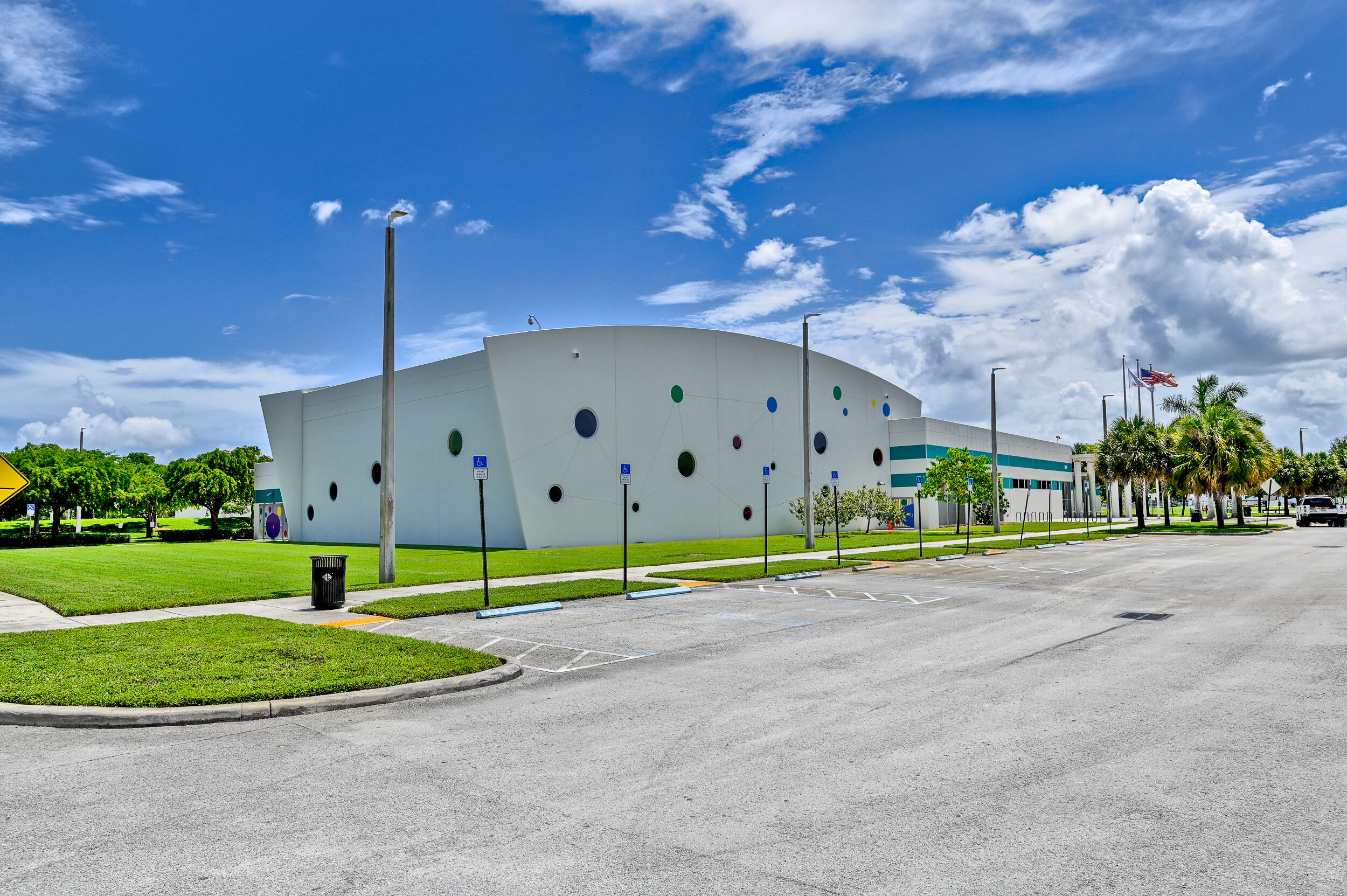 A modern building with a curved facade, parking lot, and flagpole.