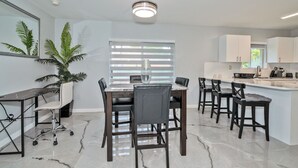 Una cucina moderna con zona pranzo, caratterizzata da un piano di lavoro in marmo, sedie in legno scuro e una ventola a soffitto.