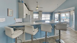 A modern kitchen with a central island, bar stools, and a ceiling fan. - Catch of the Day by Ryson Vacation Rentals (Galveston)