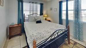 A bedroom with a bed, nightstands, a ceiling fan, and patterned curtains. - Catch of the Day by Ryson Vacation Rentals (Galveston)