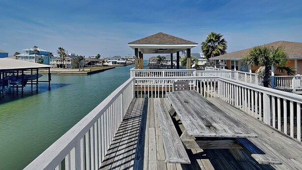 A wooden pier with a gazebo, white railings, and a view of the water and buildings in the background. - Catch of the Day by Ryson Vacation Rentals (Galveston)