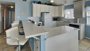 A modern kitchen with white cabinetry, a central island, and a ceiling fan. - Catch of the Day by Ryson Vacation Rentals (Galveston)