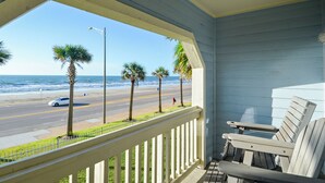 A balcony with a view of the beach and ocean, featuring a white railing and a wooden chair. - Dawn's Early Light by Ryson Vacation Rentals (Galveston)