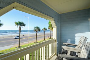 A balcony with a view of the beach and ocean, featuring a white railing and a wooden chair. - Dawn's Early Light by Ryson Vacation Rentals (Galveston)