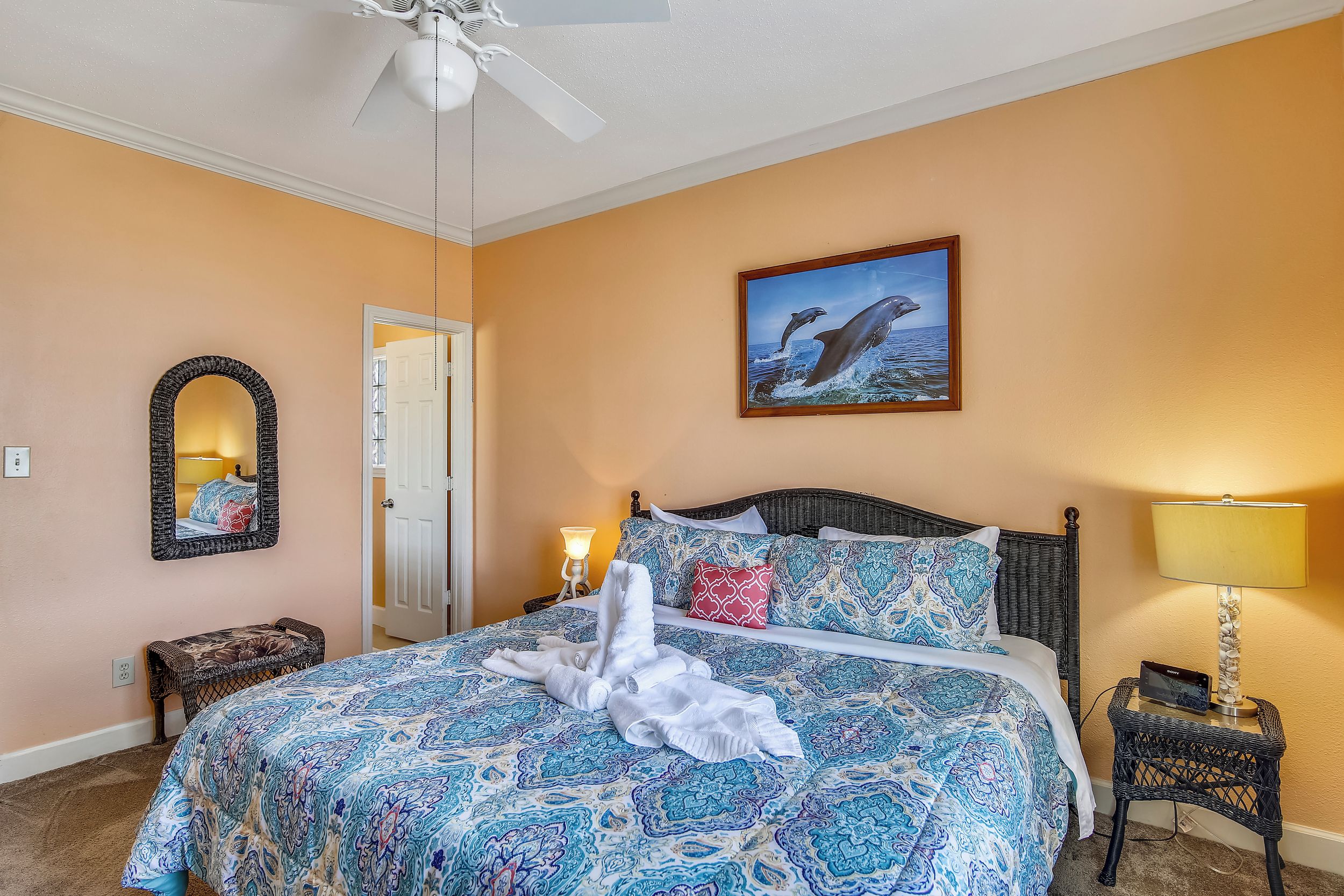 A hotel room with a bed, a nightstand, a lamp, a mirror, and a painting of dolphins.