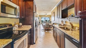 A kitchen with dark wooden cabinets, stainless steel appliances, and a granite countertop. - Dawn's Early Light by Ryson Vacation Rentals (Galveston)