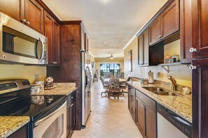A kitchen with dark wooden cabinets, stainless steel appliances, and a granite countertop. - Dawn's Early Light by Ryson Vacation Rentals (Galveston)