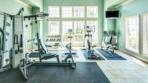 Un gimnasio con diverso equipo de ejercicio, amplias ventanas y un televisor instalado en la pared.