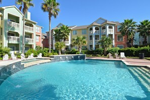 A swimming pool surrounded by multi-story buildings with balconies, palm trees, and outdoor seating areas. - Turtle Romance by Ryson Vacation Rentals (Galveston)
