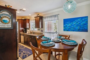 A dining area with a wooden table set for four, a kitchen with dark wood cabinets, and a decorative sign above the door.