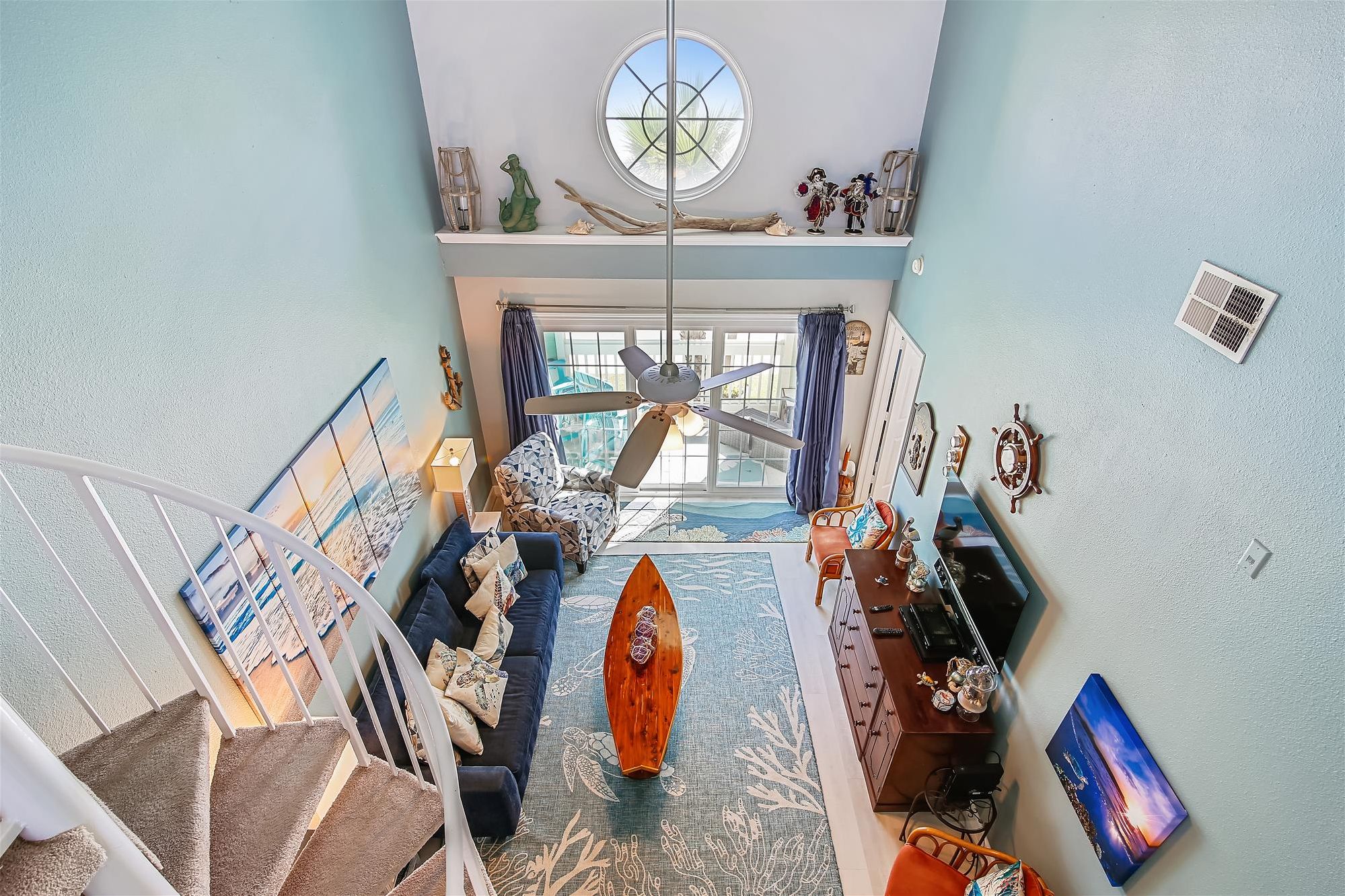 A spacious living area with a large window, a ceiling fan, and a staircase leading to an upper level.