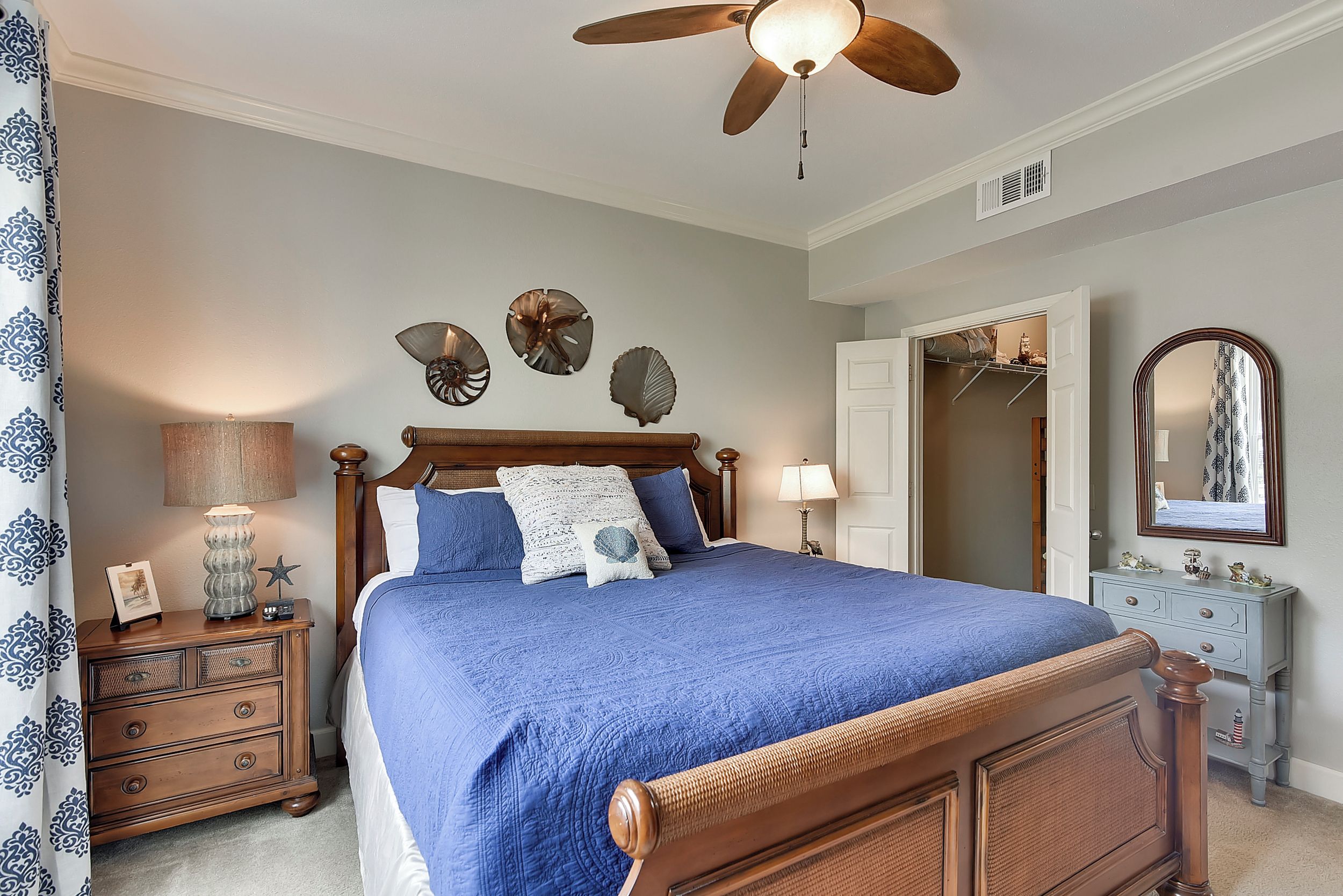 A bedroom with a wooden bed, a ceiling fan, a dresser, a mirror, and wall decorations.