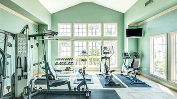 A gym with various exercise equipment, large windows, and a television mounted on the wall.